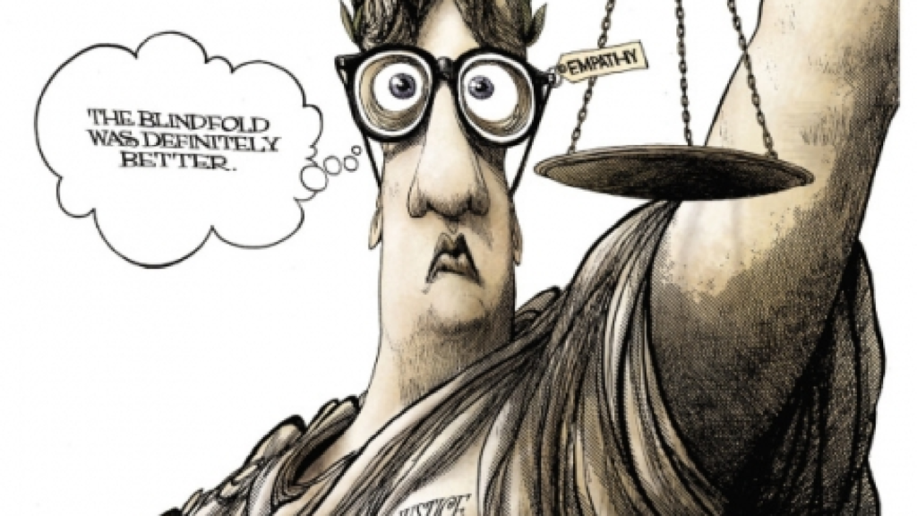 Editorial cartoon — Lady Justice, blindfold replaced by thick glasses labeled 'EMPATHY', thinking: 'The blindfold was definitely better.'